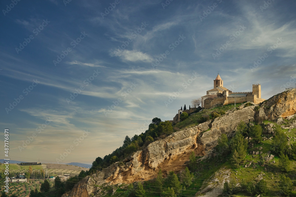 View of the Moorish castle of Iznájar (Córdoba, Spain) and the bell tower of the Christian church of Santiago Apóstol on a hill at sunset
