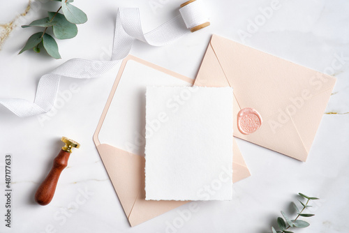 Feminine wedding invitation. Blank paper card mockup, pink envelopes, silk ribbon, eucalyptus, wax seal stamp on marble table. Wedding stationery template.