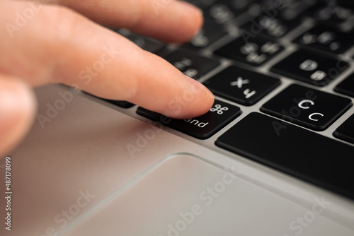Hand pressing command key on modern laptop keyboard. Command sign and symbol close-up