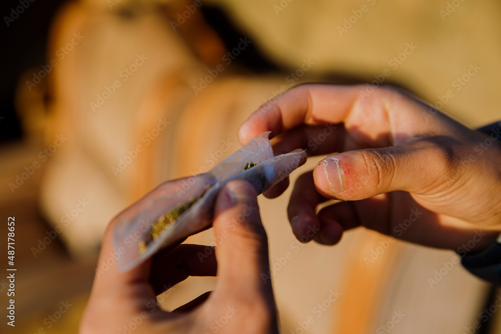 Close-up of a boy's hands rolling a marijuana joint outdoors