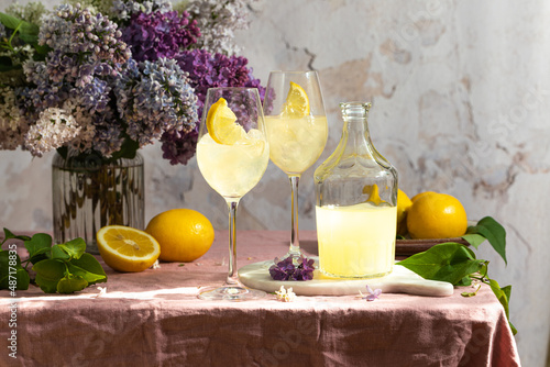 A bottle of Italian traditional liqueur limoncello with glasses, lemons and a vase with blooming lilac photo
