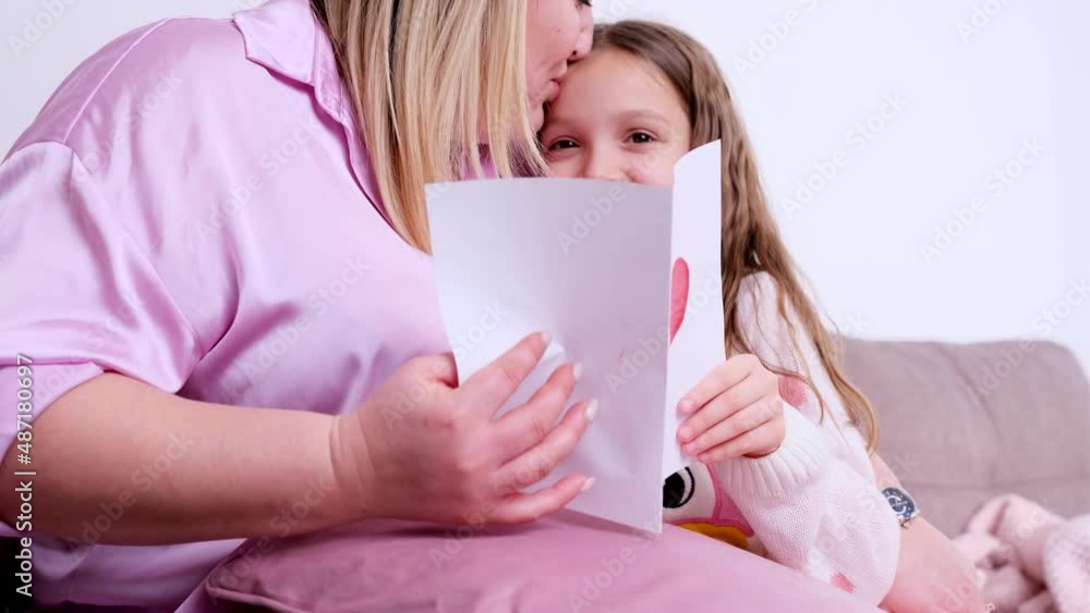 Cropped video of a little cute girl holding in her hands a present card with heart sign for her mother and giving it to her, mother kissing daughter with love. Cropped video of a little cute girl holding in her hands a present card with heart sign for her mother and giving it to her, mother kissing daughter with love.