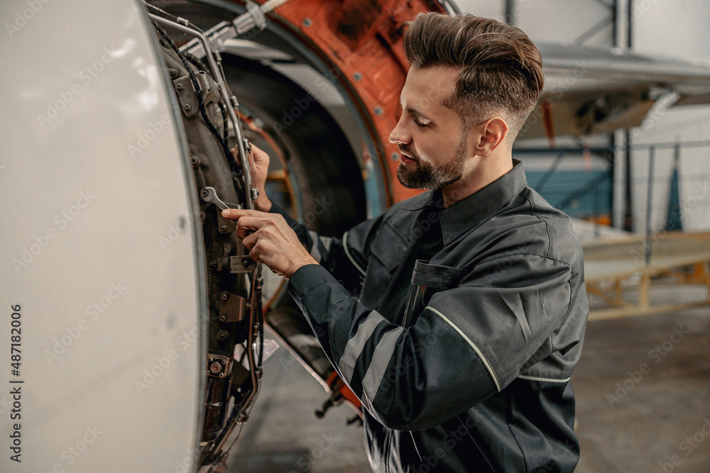 Bearded man maintenance technician tightening bolt with wrench while working at airplane repair station