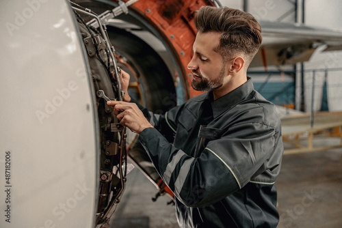 Bearded man maintenance technician tightening bolt with wrench while working at airplane repair station