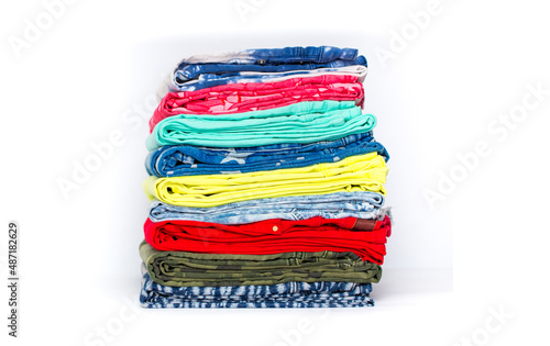 A stack of multi-colored clothing and various jeans neatly folded on a white background. Rainbow fabrics for sewing, close-up. Fashion and style, casual wear.