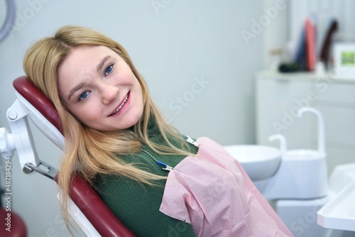 Portrait of happy positive cheerful blonde European girl  young satisfied smiling woman patient with perfect smile is lying  having a seat in medical chair in dental office after treatment in clinic.