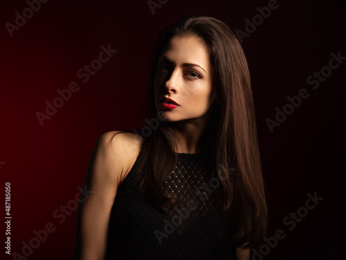 Beautiful bright makeup woman with red lipstick with half face in shadow on dark red background with empty copy space. Closeup