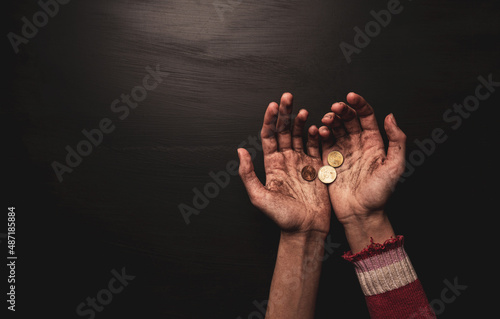 Poverty - kid begging for money. Dirty skinny beggar child’s hands with coins on black. photo