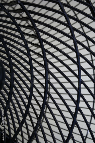 Parrilla negra con curvas para protecciòn de paletas de ventilador industrial, forma un diseño abstracto con fondo claro