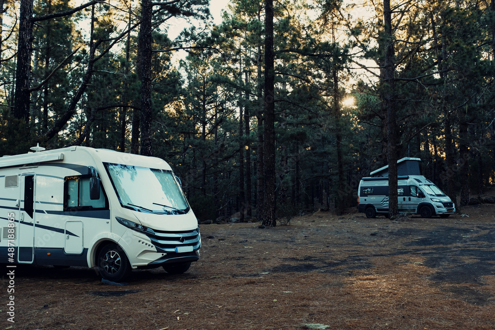 Two camper van parked in the wild with forest woods and trees all around. Concept of alternative vanlife lifestyle and transport vehicle holiday leisure vacation