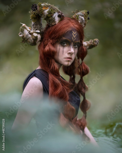 Girl with faun horns covered with moss in the forest