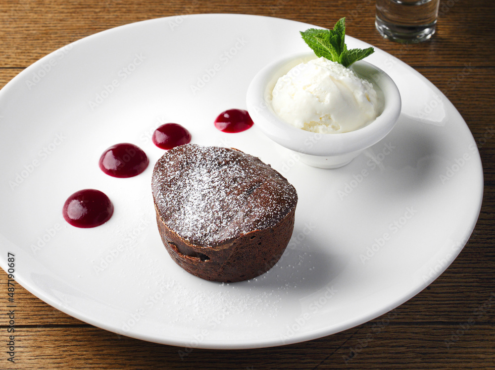 Lava cake made of chocolate lipstick with berry sauce and ice cream with mint leaf. Serving a delicious chocolate dessert in a cafe, restaurant. Sweet cupcake with ice cream for a child. Copy space. Lava cake made of chocolate lipstick with berry sauce and ice cream with mint leaf. Serving a delicious chocolate dessert in a cafe, restaurant. Sweet cupcake with ice cream for a child. Copy space.