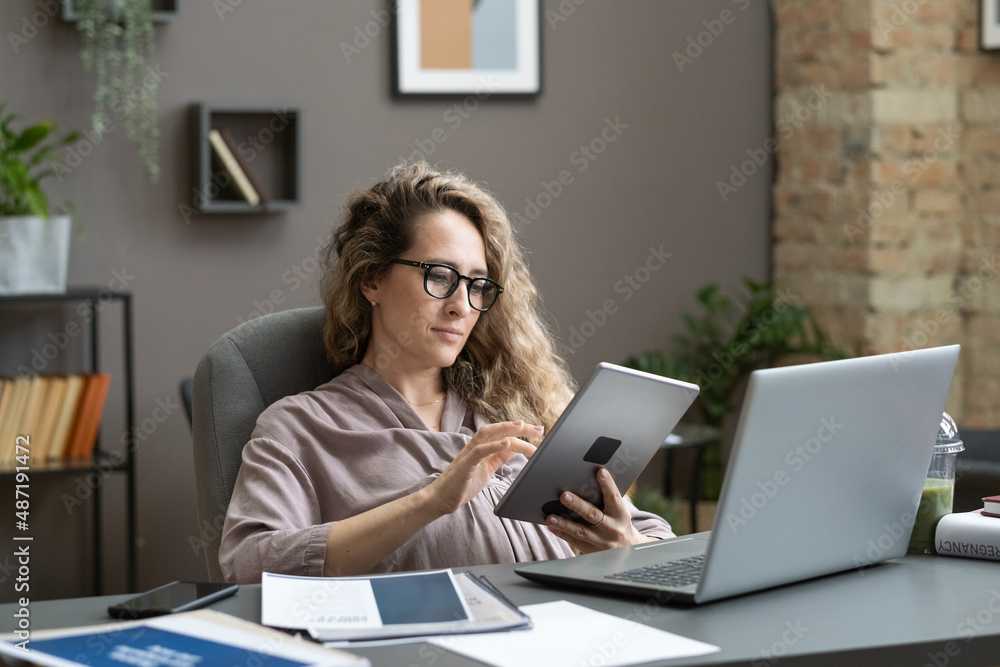 Young pregnant employee doing online work on digital tablet while sitting at the table with laptop at office Young pregnant employee doing online work on digital tablet while sitting at the table with laptop at office