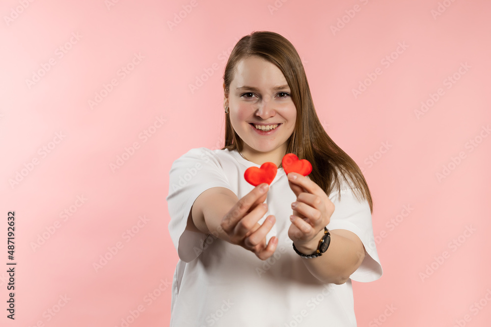 Smiling young girl with brown hair in a white t-shirt on a pink background and red hearts. High quality photo Smiling young girl with brown hair in a white t-shirt on a pink background and red hearts. High quality photo