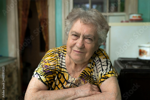 Close-up portrait of a poor elderly woman in the kitchen at home. 