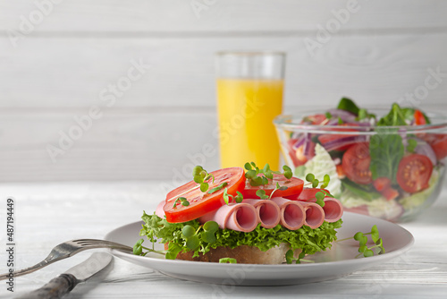 Sandwich with sausage and tomatoes, with salad and orange juice. European breakfast.
