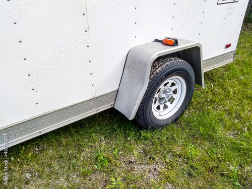 white cargo trailer with dented fender parked on grass, tire rim 