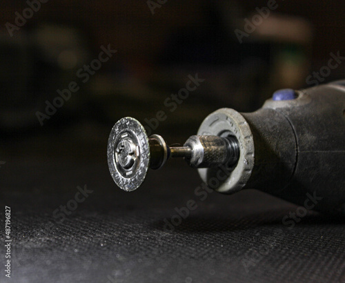 Dremel, an American brand of power tools. Multifunctional, rotating tool with a nozzle isolated on a dark background close-up. Grey rotating multifunctional tool with inserted grinding disc.