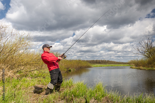Fisher with a fishing rod stands on the river bank.