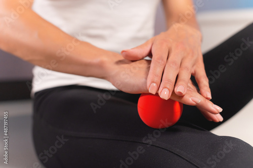 Close-up of a caucasian woman giving herself a myofascial thigh massage with a massage red ball