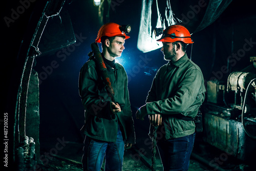 Two tired young miners in an old coal mine communicate with each other at work. Miners in a protective suit with a helmet on their heads and a flashlight stand in a cold tunnel.