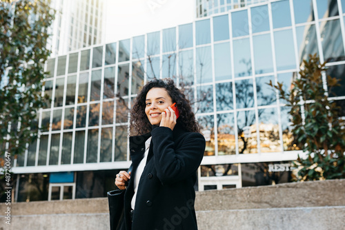 Young businesswoman talking on a red smartphone on the street