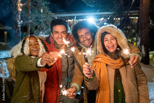 Canvas Print Portrait of happy friends smiling at camera standing outdoors with sparklers in
