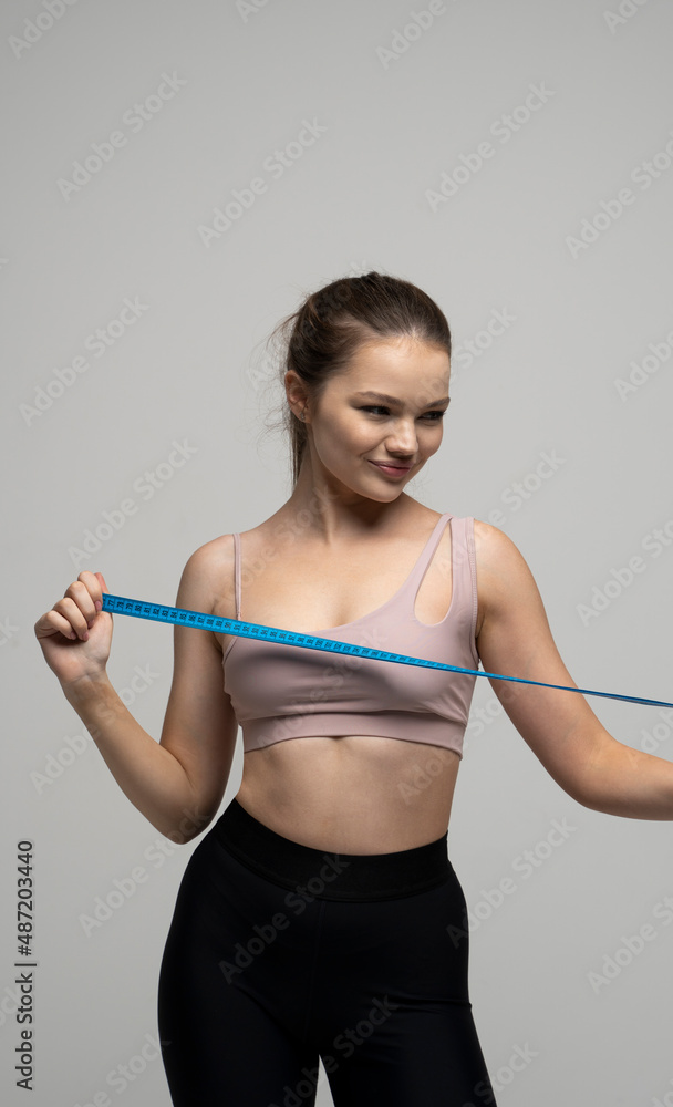 Happy attractive brunette woman with a perfect sexy body in beige top sportswear holding a blue measuring tape. Weight loss and diet concepts. Health care and healthy nutrition. Perfect slim body.
