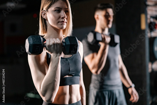 A muscular woman exercising with weights in a gym with her partner.