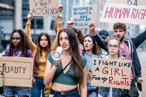Young woman with megaphone leading a multiracial group of people in a stike for equality and women rights, activits in protest in the city photo