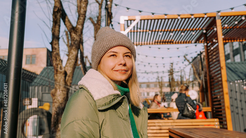 Smiling blonde woman sitting at a table in an urban space street cafe with street food. Warm winter day to meet friends