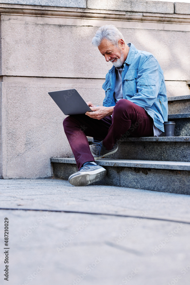 A senior student sits on the stairs of the university building and uses his laptop to look at notes before an exam. A senior student sits on the stairs of the university building and uses his laptop to look at notes before an exam.