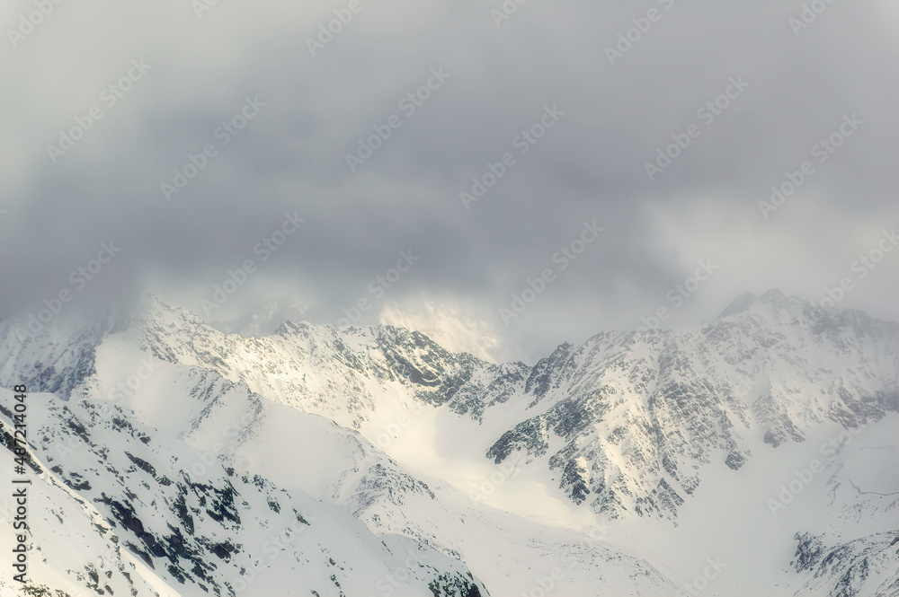 Snow covered Alps peak with cloudy sky background during winter day.