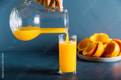 An anoymous hand is filling fresh orange juice to glass photo