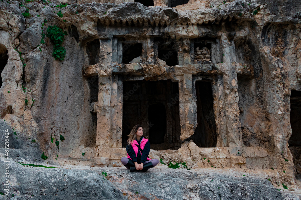 Tlos ancient city from Fethiye, Turkey. Young girl is sitting on rocks. She is looking side. She wears pink winter clothes. Tlos ancient city from Fethiye, Turkey. Young girl is sitting on rocks. She is looking side. She wears pink winter clothes.