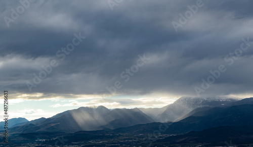 Sun ligths coming between clouds to snowy mountain. A sharp light seems on the photo. Amazing view.