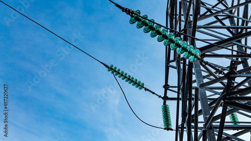Close up of a transparent turquoise high voltage insulator or isolator in sunlight on electric tower on blue sky background. Electric power transmission line
