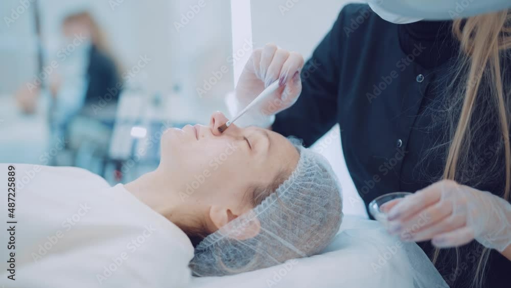 Beautician applying cream to face of woman patient with closed eyes. Concept of care and youth Beautician applying cream to face of woman patient with closed eyes. Concept of care and youth