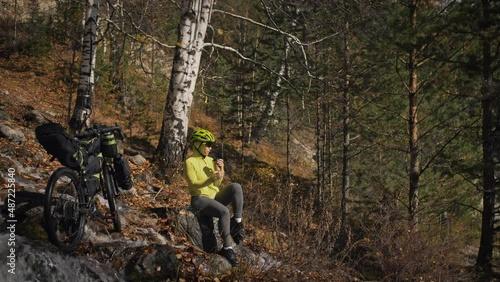 The woman travel on mixed terrain cycle touring with bikepacking. The traveler journey with bicycle bags. Sportswear in green black colors. The trip in magical autumn forest, river stream. photo