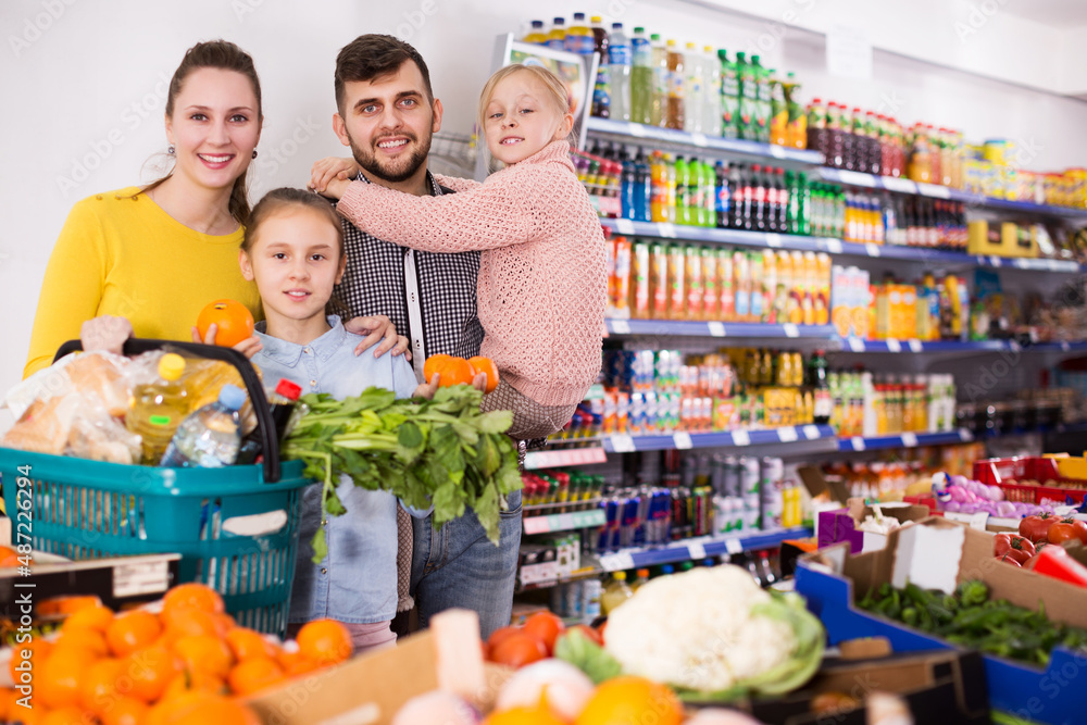 Obraz premium Two small positive sisters during family shopping in greengrocery department of supermarket