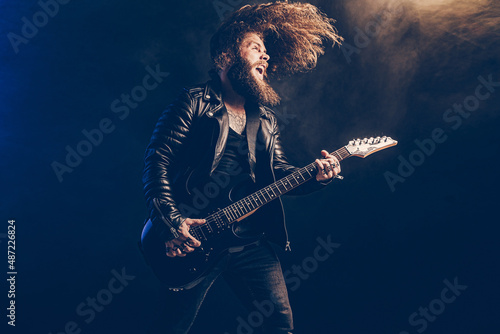 Emotional man rock guitar player with long hair and beard plays on the smoke background. Studio shot