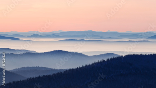 Mountain range with visible silhouettes through the morning colorful fog. Beautiful mountain background. © MariaSh