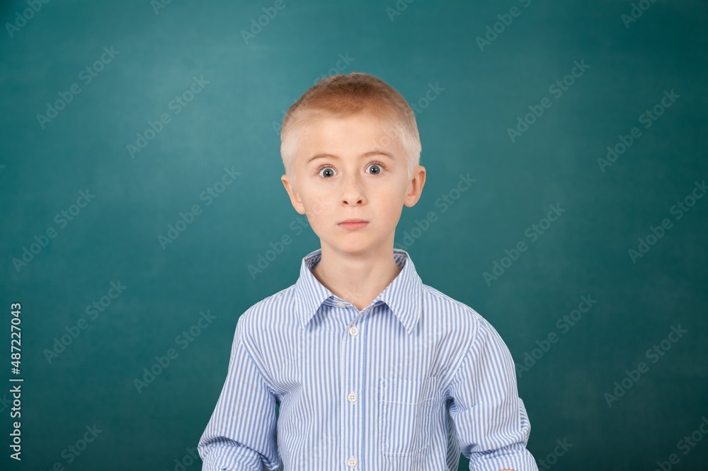 Happy cute kid boy school student looking at camera at blackboard background.
