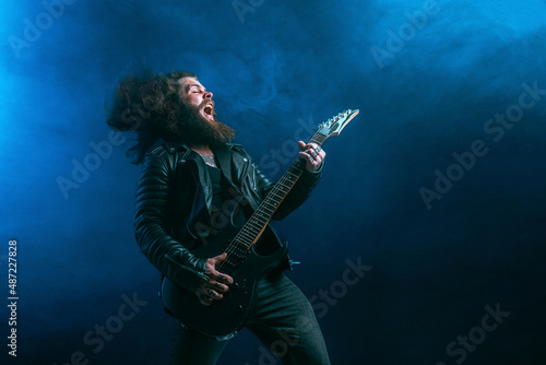 Emotional man rock guitar player with long hair and beard plays on the smoke background. Studio shot