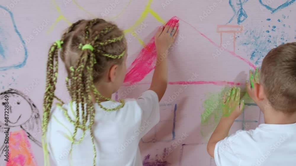 A little girl and a boy preschoolers paint with their hands on a wall ...