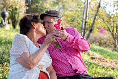 Beautiful old couple being romantic in nature. Elderly man giving a flower to his wife and kissing her.