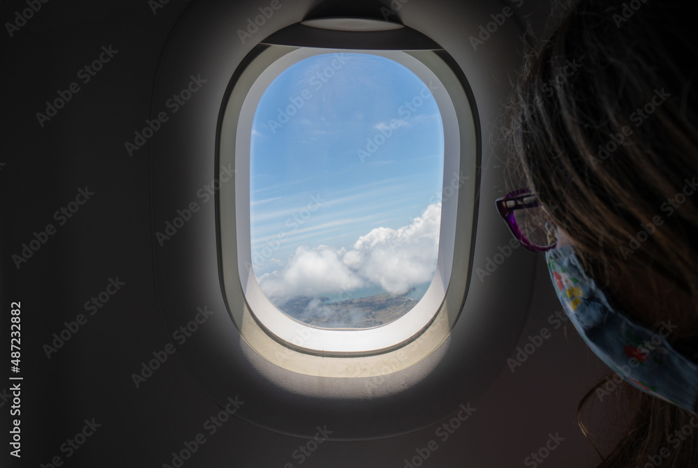 Young Girl Looking Out Airplane Window Over Ocean and Clouds on a Sunny Day at Take Off Young Girl Looking Out Airplane Window Over Ocean and Clouds on a Sunny Day at Take Off