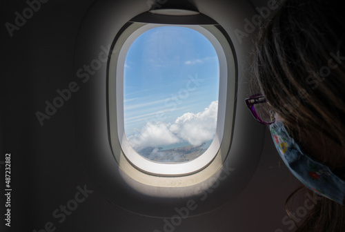 Young Girl Looking Out Airplane Window Over Ocean and Clouds on a Sunny Day at Take Off