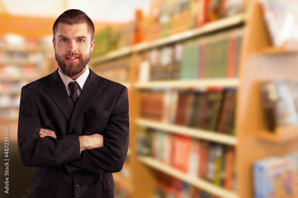 Mature professor standing with arms crossed in a library and posing Mature professor standing with arms crossed in a library and posing