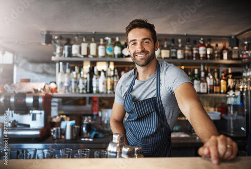 Drinks on me. Portrait of a confident young man working behind a bar counter.